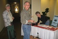 Suzanne Stedman helping Doug Olsen check in for fiddle and mandolin workshop and David Belcher check in for fiddle workshop.